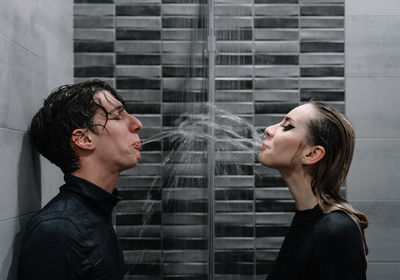 Young couple spitting water at each other in shower