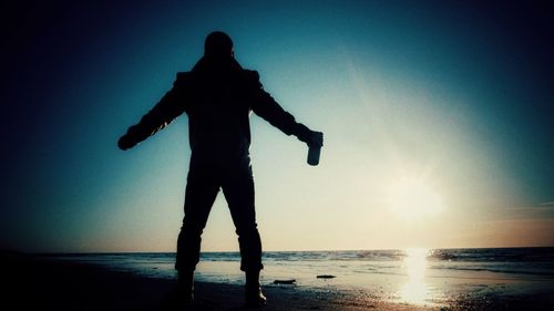 Silhouette man standing on beach against bright sun