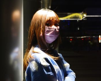 Portrait of young woman standing against illuminated city at night