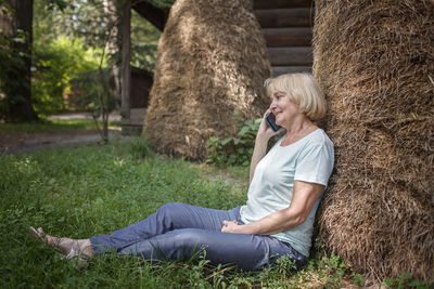 Full length of woman sitting on mobile phone in grass