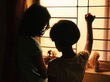 Rear view of friends standing against window at home