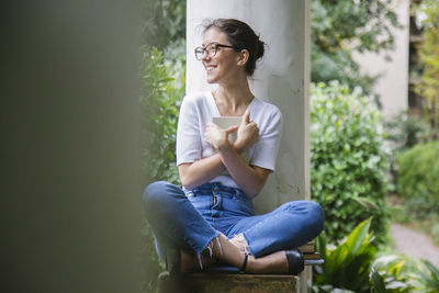 Full length of young woman using phone while sitting outdoors