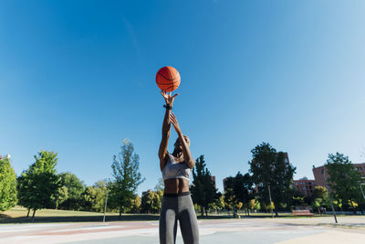 Basketball player throwing ball on sunny day