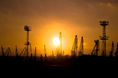 Silhouette cranes against sky during sunset