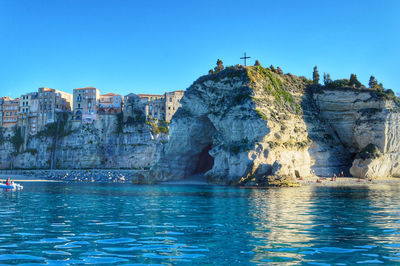 Rock formations by sea against clear blue sky