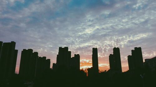 Low angle view of silhouette buildings against cloudy sky