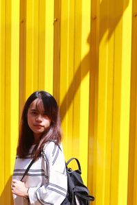 Portrait of woman standing against yellow corrugated wall