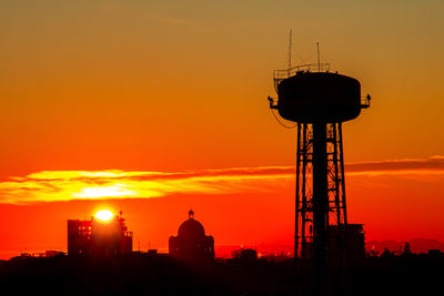 Silhouette water tower against orange sky