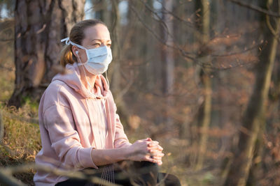 Woman wearing mask sitting in forest