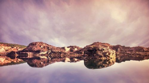 Rock formations reflecting on calm lake against cloudy sky
