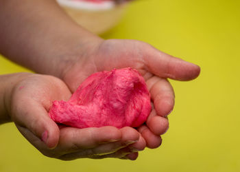 Close-up of hand holding red rose over yellow background