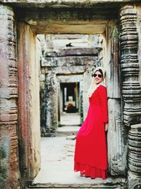 Portrait of woman wearing red evening gown while standing at old ruins