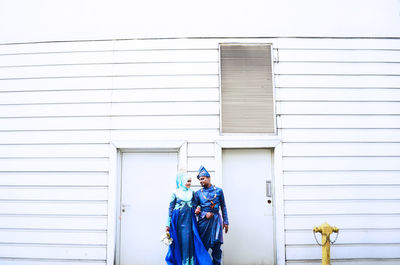 Full length of bride and groom standing in front of building