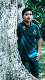 Portrait of young man standing against tree trunk