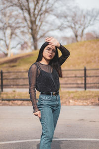 Young woman shielding eyes while standing on road in city