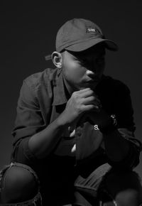 Portrait of young man holding hat against black background