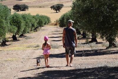 Rear view of girl and father with dog standing on footpath against trees