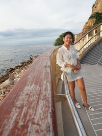 Portrait of woman standing on railing by sea against sky