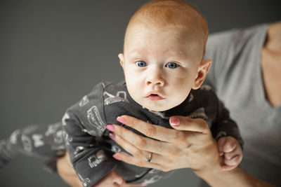 A close-up portrait of a newborn baby boy, which the mother holds on her arms,gray background