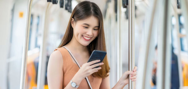 Smiling woman using mobile phone while traveling in subway train