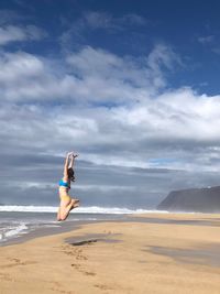 Woman jumping on beach against sky