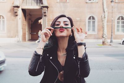 Portrait of beautiful woman making mustache while standing against building