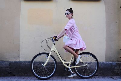 Full length of woman cycling on road by wall