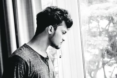 Thoughtful young man looking through window at home