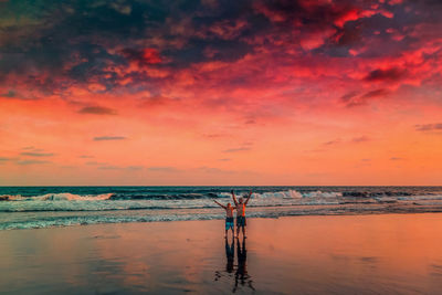 Shirtless male friends standing at beach against orange sky