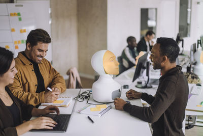 Happy phd students planning by robot at desk in innovation lab