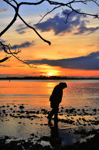 Silhouette man standing on beach against sky during sunset