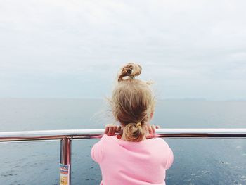 Rear view of girl standing by railing at sea against sky