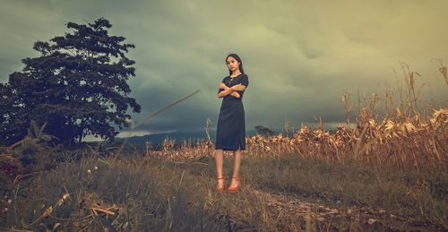 Full length of young woman standing on field against cloudy sky during sunset