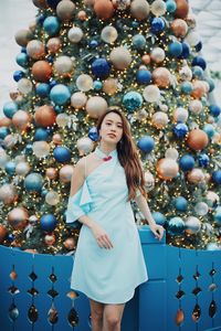 Portrait of smiling young woman standing by christmas tree outdoors