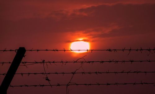 Silhouette fence against orange sky during sunset