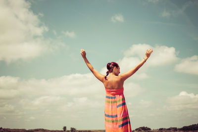 Rear view of carefree woman with arms outstretched against the sky. copy space.