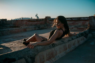 Woman sitting on retaining wall against sky