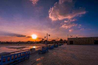 City street by sea against sky during sunset