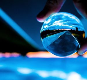 Close-up of hand holding crystal ball against blue sky