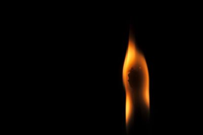 Close-up of burning candle against black background