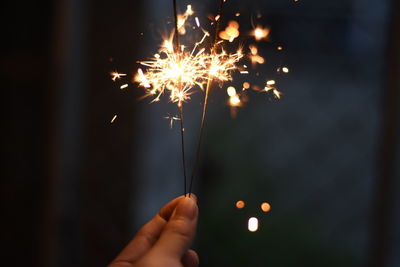 Cropped hand holding lit sparkler at night