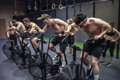 Athletes cycling on exercise bike with women standing in background at gym