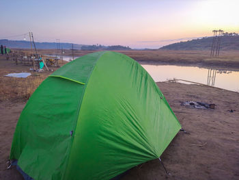 Isolated camping tent at calm lake shore with dramatic sunrise colorful sky reflection at morning