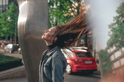 Side view of young woman tossing hair while standing on road in city