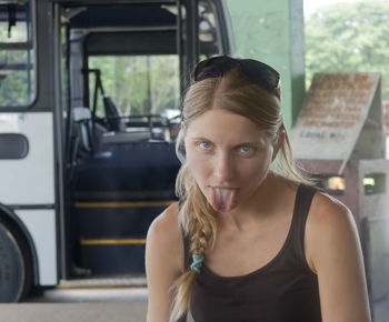 Portrait of young woman sticking out tongue against parked bus