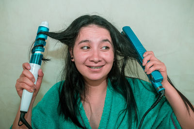 Close-up of young woman holding curling tongs and hair straightener