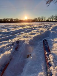 Snow covered field against sky during sunset