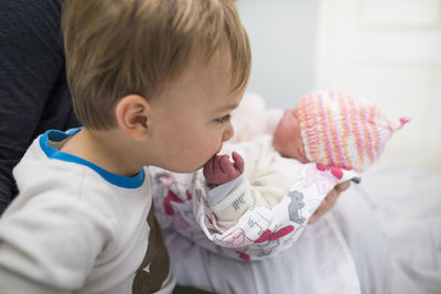 Cute brother kissing newborn sister's hand carried by mother at home