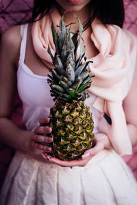 Midsection of woman holding pineapple while standing against pink wall