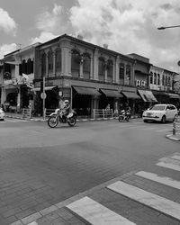 Cars on city street by buildings against sky